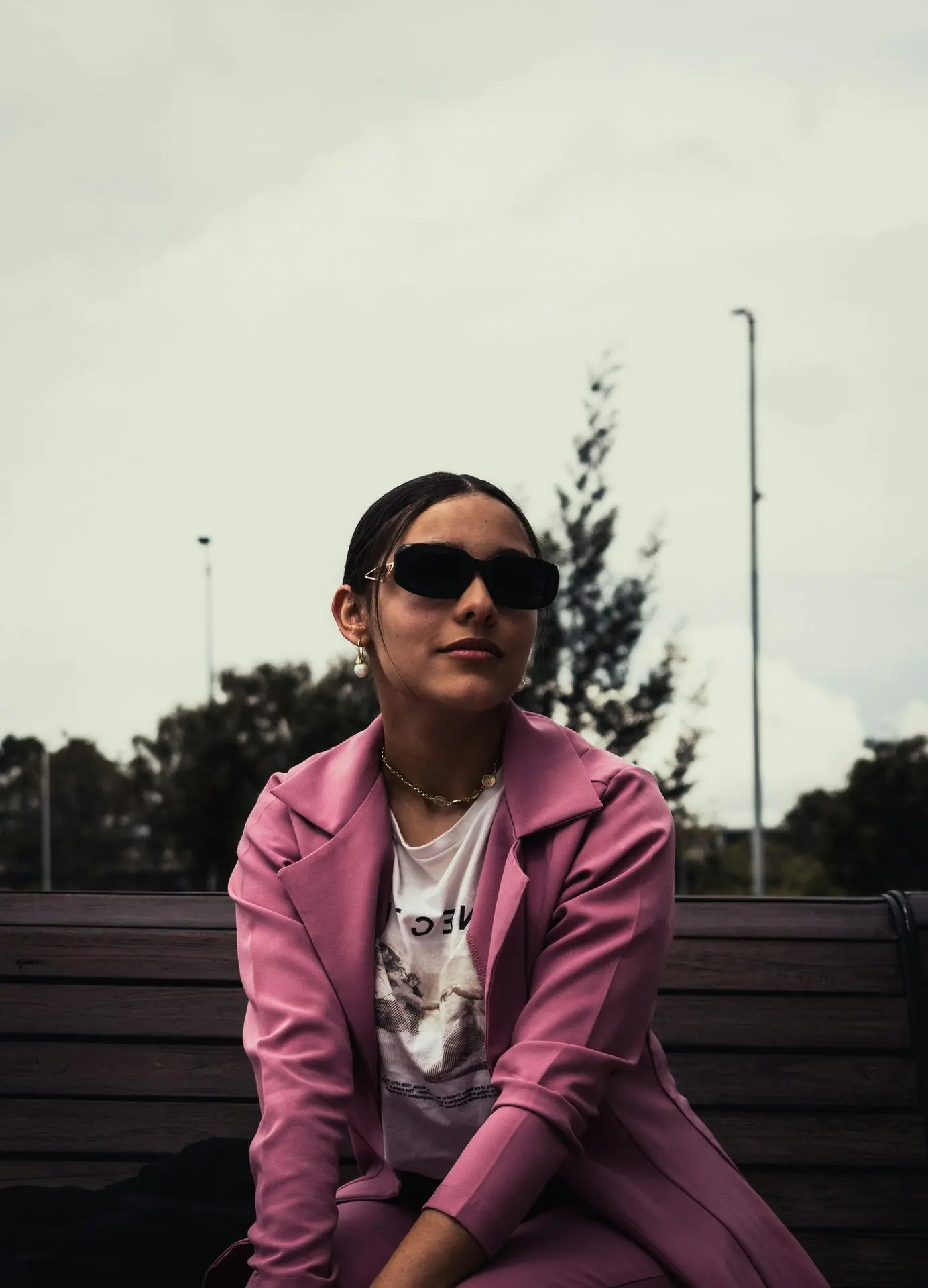 a woman in a pink coat and sunglasses sitting on a bench